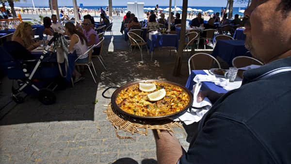 Kelner niosący paellę w barze na plaży na wybrzeżu śródziemnomorskim w Hiszpanii.